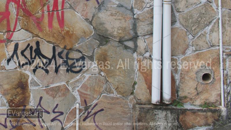 street wall with graffiti, rocks on the wall, white plastic pipes, day, outdoors